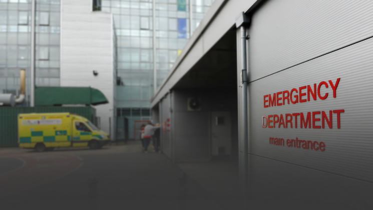 The front of an emergency department with an ambulance in the background