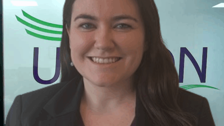 A woman stands in front of the UNISON logo in an office