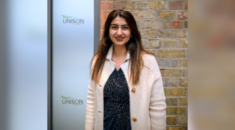 A young woman stands in front of a brick wall and glass doors with the UNISON logo in the background